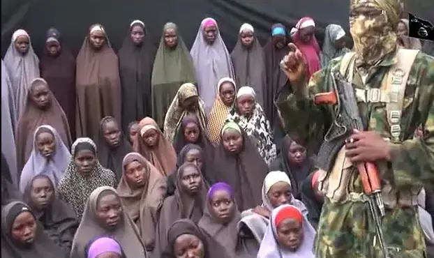 A Boko Haram soldier with an AK-47, speaking in front of young female hostages dressed in Muslim attire