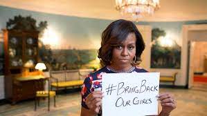 Michelle Obama, in the White House, with a look of disappointment, holding a sign #BringBackOurGirls