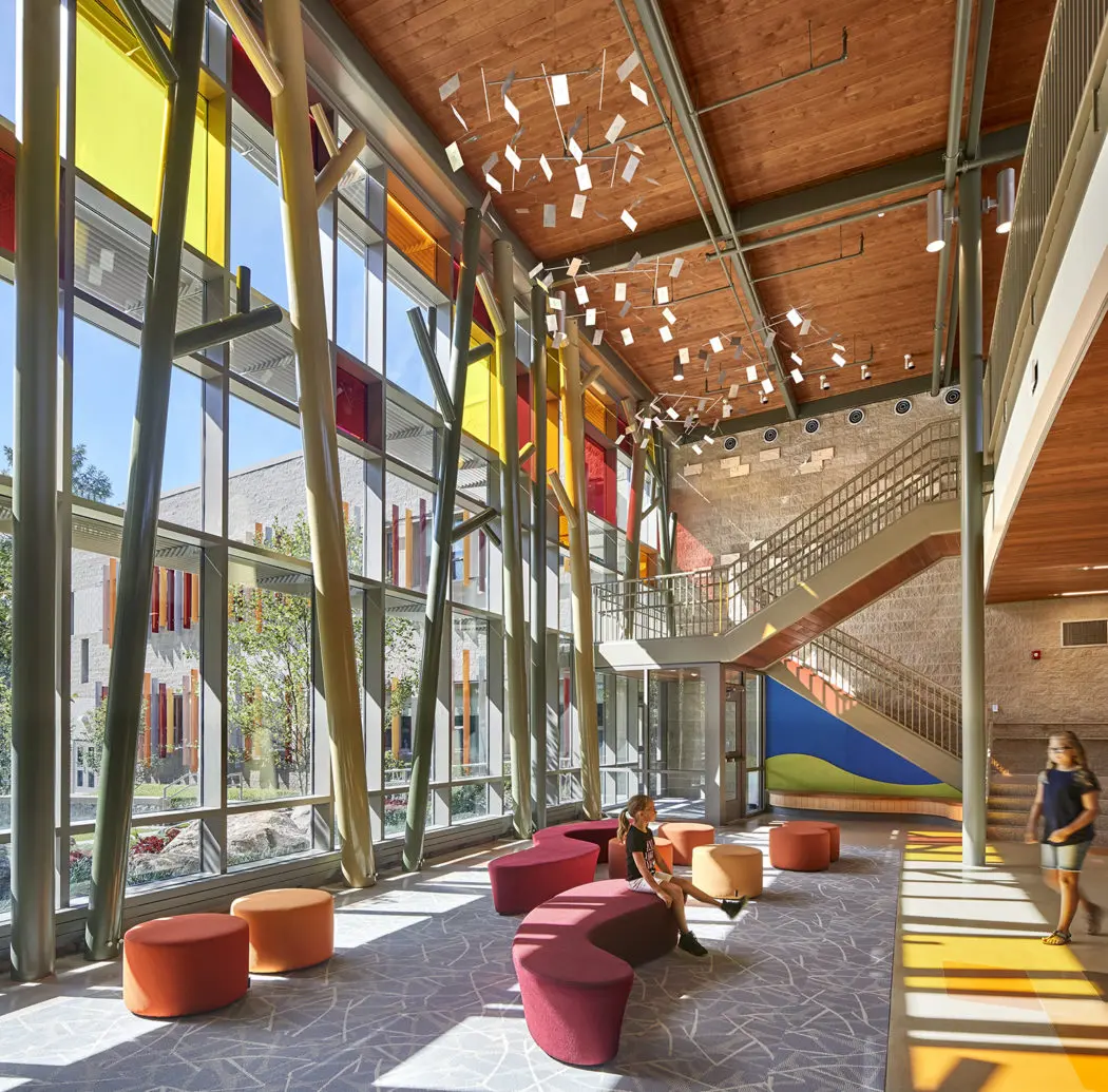 Sunlight shines into a furnished foyer through a wall of windows featuring intermittent stained-glass panels