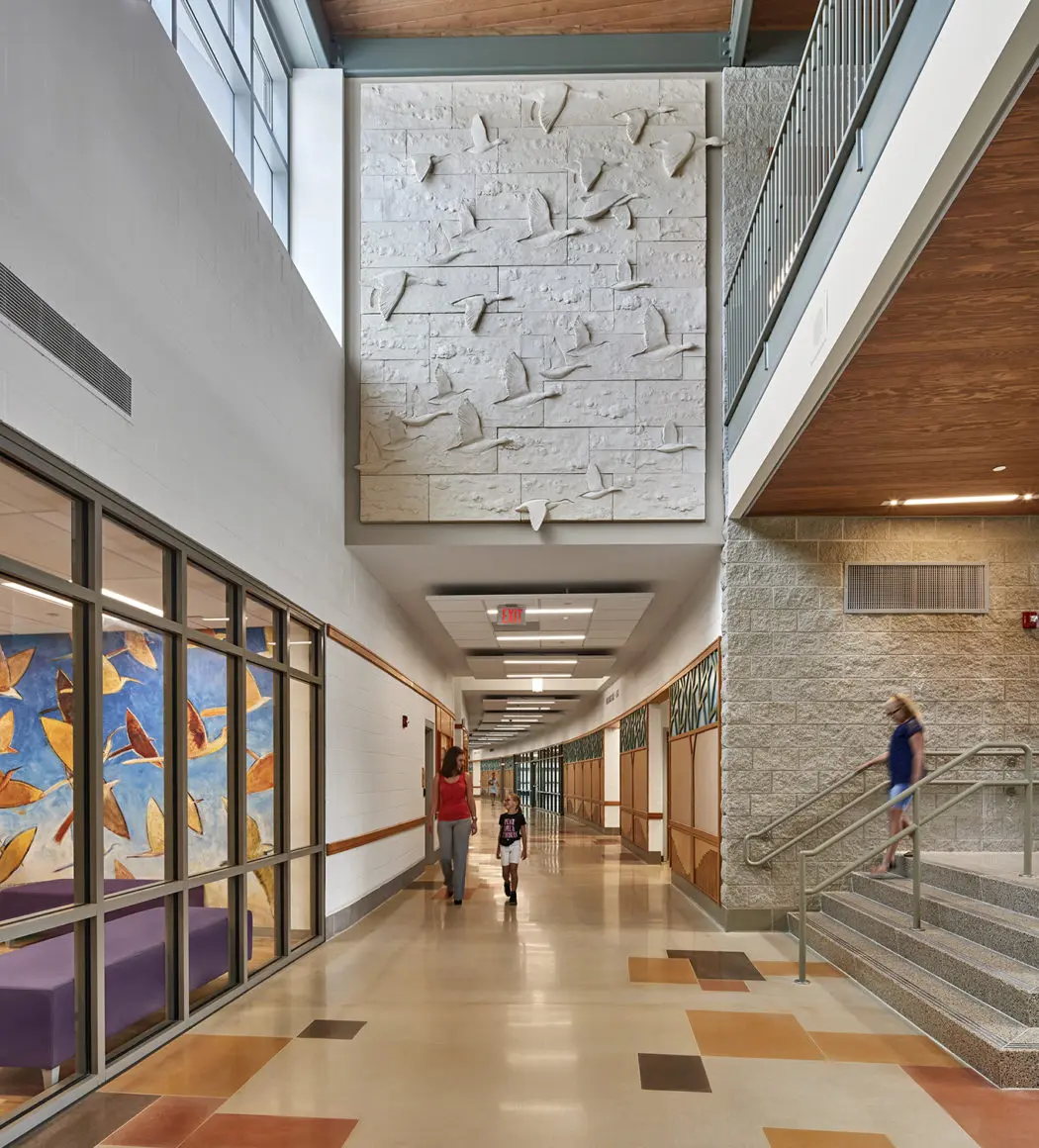 A curved hallway with scattered colourful squares continues past some some concrete steps with bare steel hand-rails